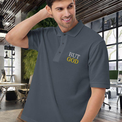 White man wearing a dark gray polo shirt. On the top left corner, there is an embroidered design that says &quot;BUT GOD&quot; in caps lock. This shirt is sold at Amela&