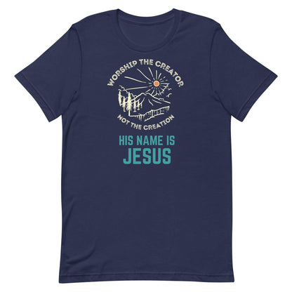 Flatlay of a blue Christian t-shirt. There is a graphic of a mountain, trees, and sun. Over the graphic, it says &quot;Worship the creator&quot;, and under it says &quot;not the creation&quot;. On the bottom, it says &quot;His name is Jesus&quot;. This shirt is sold at Amela&