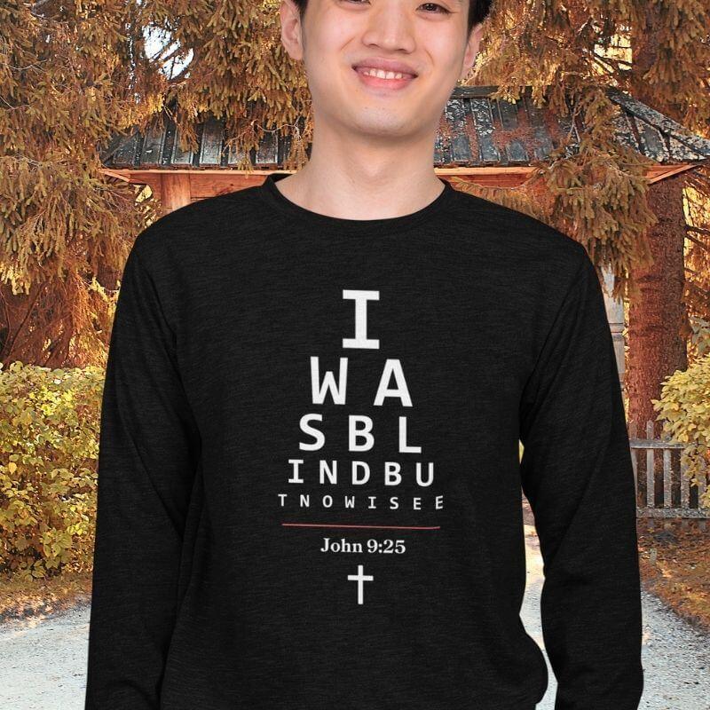 Asian man wearing a long-sleeve black Christian shirt. 

The graphic is text as an eye chart, and it says &quot;I WAS BLIND BUT NOW I SEE&quot;.

Below the text, there is a thin line, with text &quot;John 9:25&quot; and an icon of a cross below.