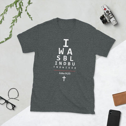 Flatlay of a gray Christian t-shirt. 

The graphic is text as an eye chart, and it says &quot;I WAS BLIND BUT NOW I SEE&quot;.

Below the text, there is a thin line, with text &quot;John 9:25&quot; and an icon of a cross below.