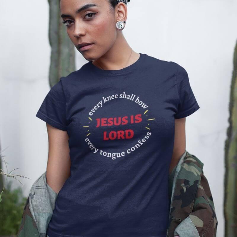 Black woman wearing navy Christian unisex T-shirt that says in a circle &quot;Every knee shall bow, every tongue confess&quot; with &quot;Jesus is Lord&quot; in the middle