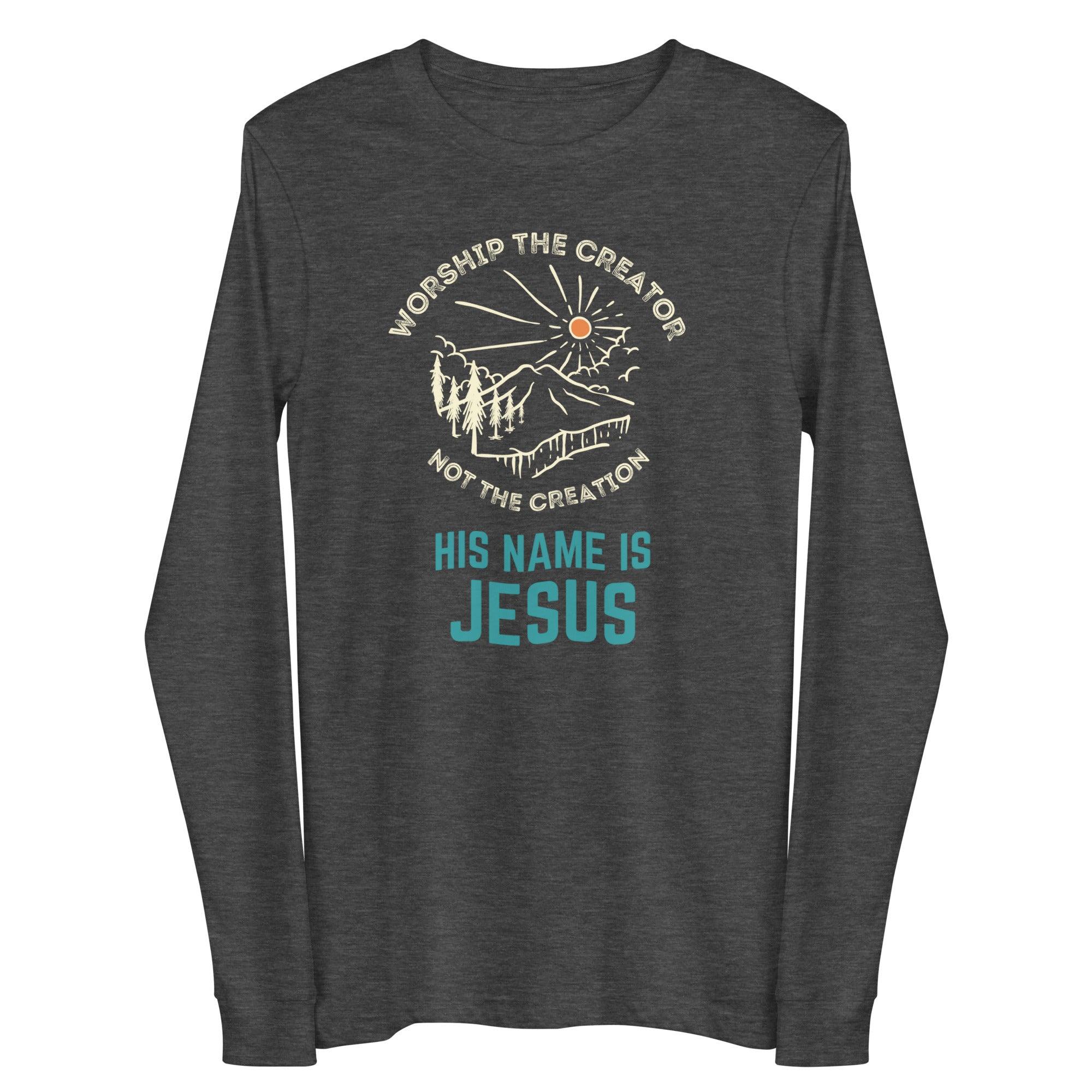 Flatlay of a grey long sleeve Christian shirt. There is a graphic of a mountain, trees, and sun. Over the graphic, it says &quot;Worship the creator&quot;, and under it says &quot;not the creation&quot;. On the bottom, it says &quot;His name is Jesus&quot;. This shirt is sold at Amela&