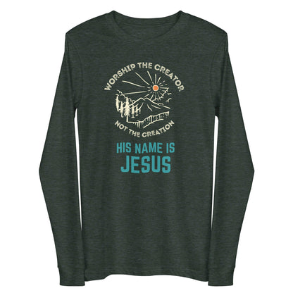 Flatlay of a pine green long sleeve Christian shirt. There is a graphic of a mountain, trees, and sun. Over the graphic, it says &quot;Worship the creator&quot;, and under it says &quot;not the creation&quot;. On the bottom, it says &quot;His name is Jesus&quot;. This shirt is sold at Amela&